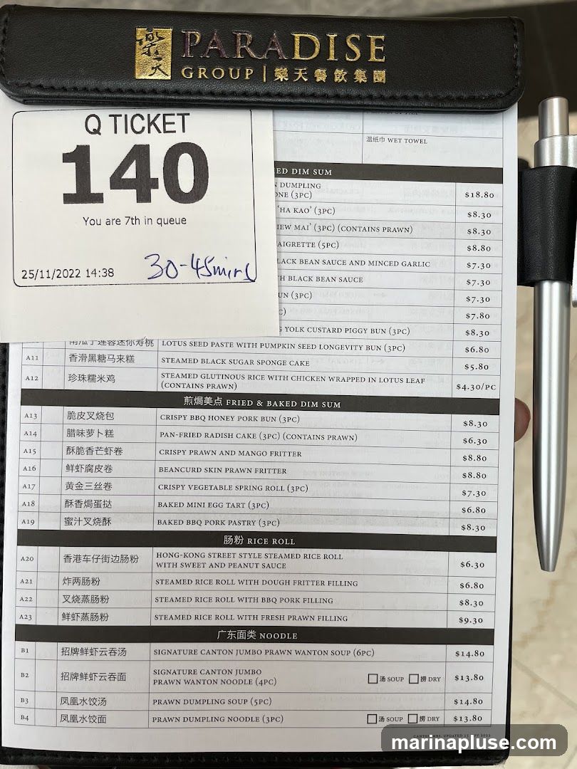 A queue ticket with the number 140 and an estimated wait time of 30-45 minutes is placed on top of a menu. The menu features various dim sum, rice rolls, and noodle dishes.
