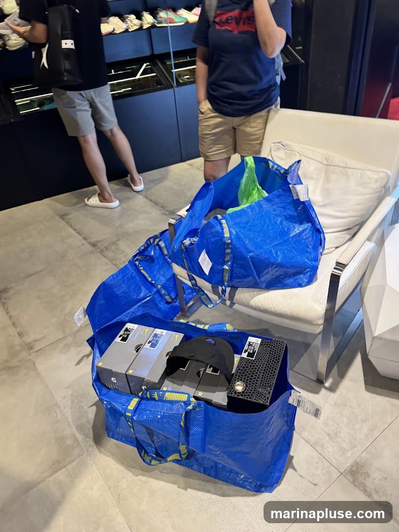 Several large blue IKEA shopping bags are filled with various items, including shoeboxes and a black baseball cap. The bags are placed on the floor and on a white armchair. In the background, two people are standing, and shelves display rows of shoes.