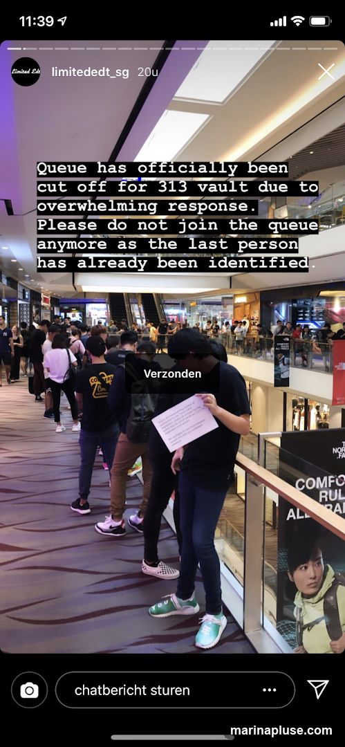 A crowd of people are standing in a long queue inside a shopping mall. A sign is being held up by one person in the queue, and a text overlay on the image announces that the queue has been cut off due to overwhelming response.