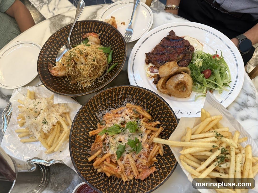 A table laden with several dishes, including pasta with shrimp, a steak with salad and onion rings, and two servings of french fries. One serving of fries is topped with grated cheese. The dishes are arranged on a marble-patterned table.