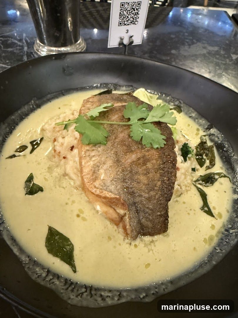 A close-up shot of a piece of salmon fillet served in a creamy sauce with rice and garnished with cilantro. A QR code table marker is visible in the background.