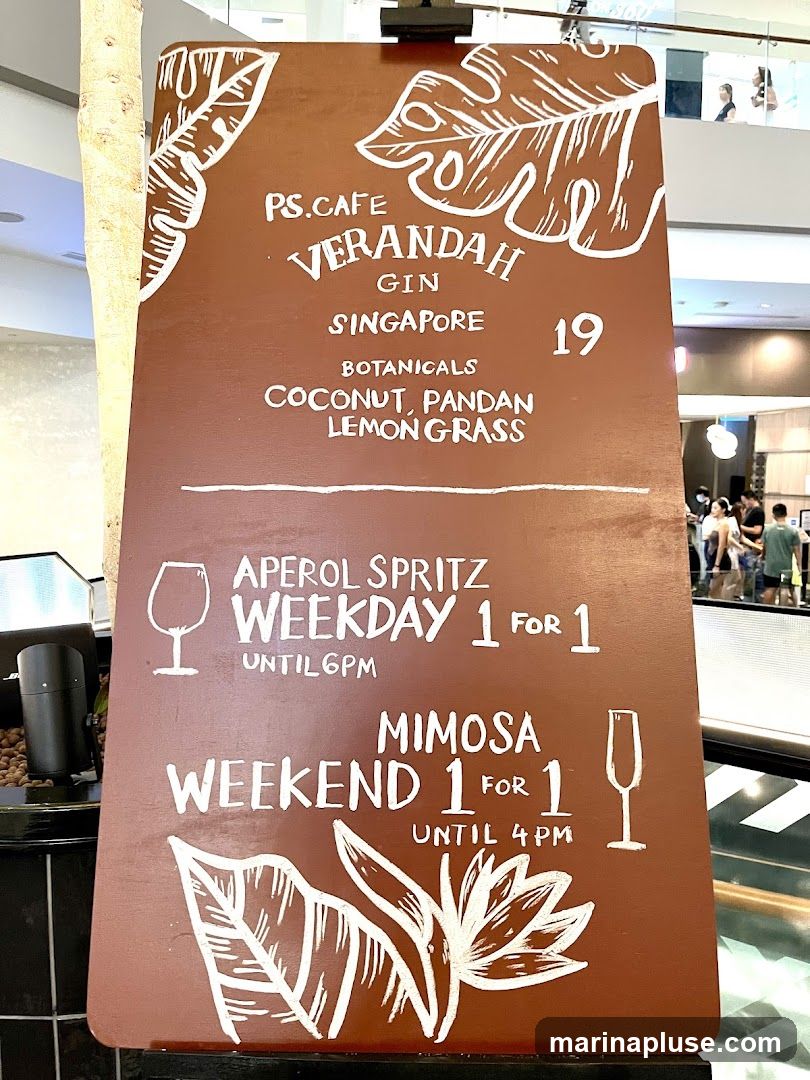 A brown menu board with white hand-drawn text and illustrations of leaves and flowers. It advertises a special on Verandah Gin and drink promotions.
