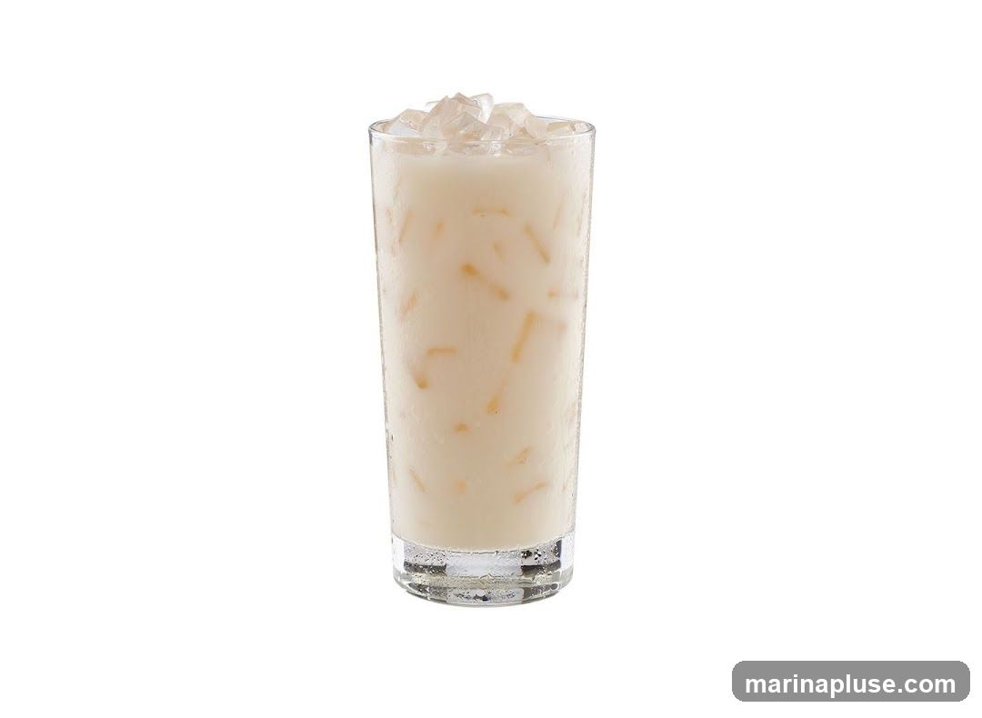 A tall glass of iced milk tea with ice cubes, against a white background.