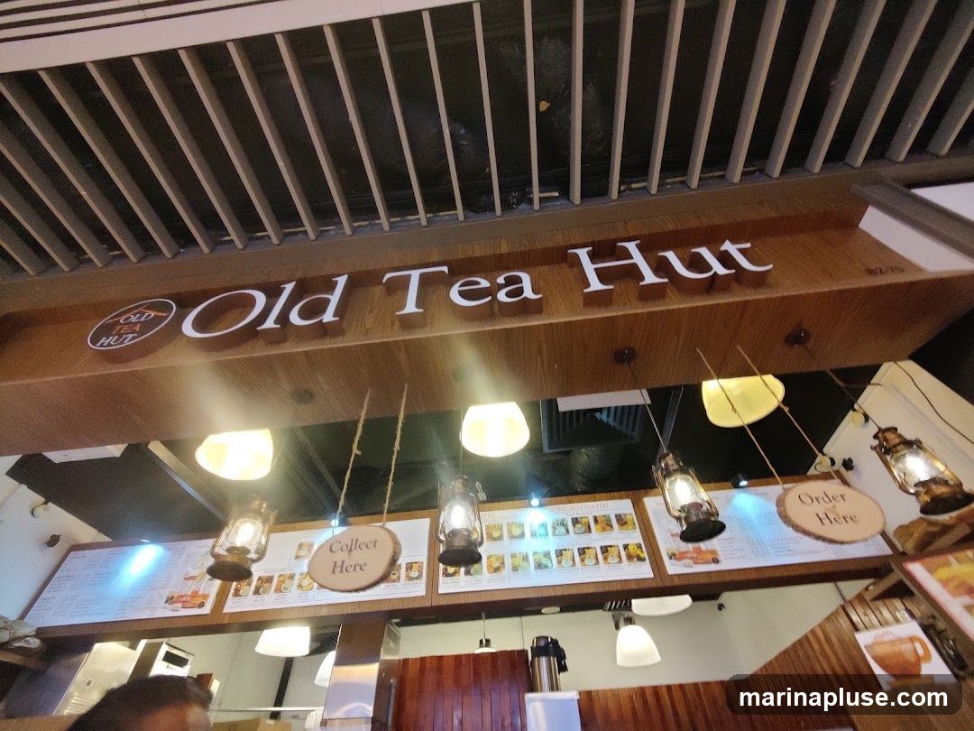 A view of the interior of Old Tea Hut, showing the prominent signage "Old Tea Hut" above a display of menus and decorative lanterns. There are also signs indicating "Collect Here" and "Order Here".