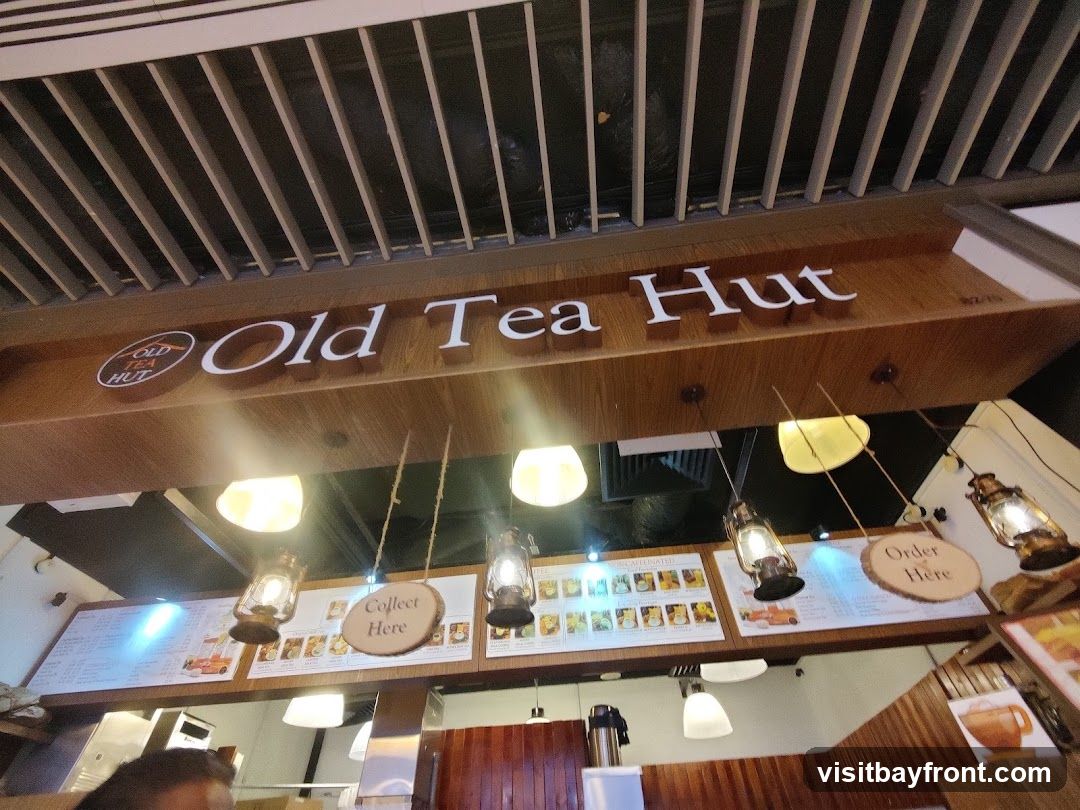 A view of the interior of Old Tea Hut, showing the prominent signage "Old Tea Hut" above a display of menus and decorative lanterns. There are also signs indicating "Collect Here" and "Order Here".