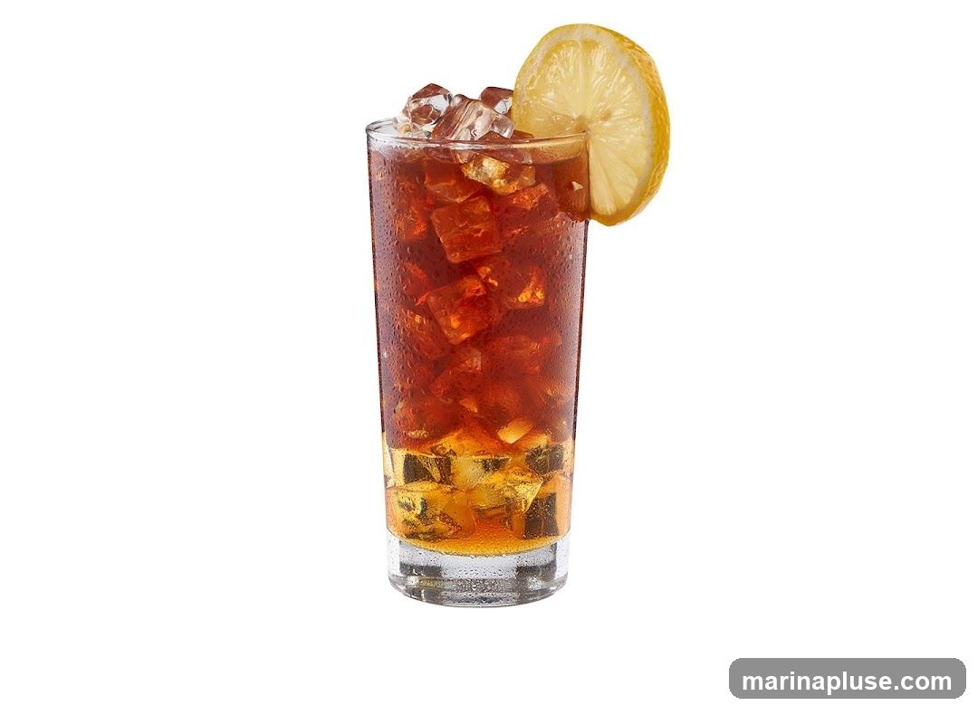 A tall glass filled with iced tea, ice cubes, and a slice of lemon on the rim. The glass has condensation on the outside.