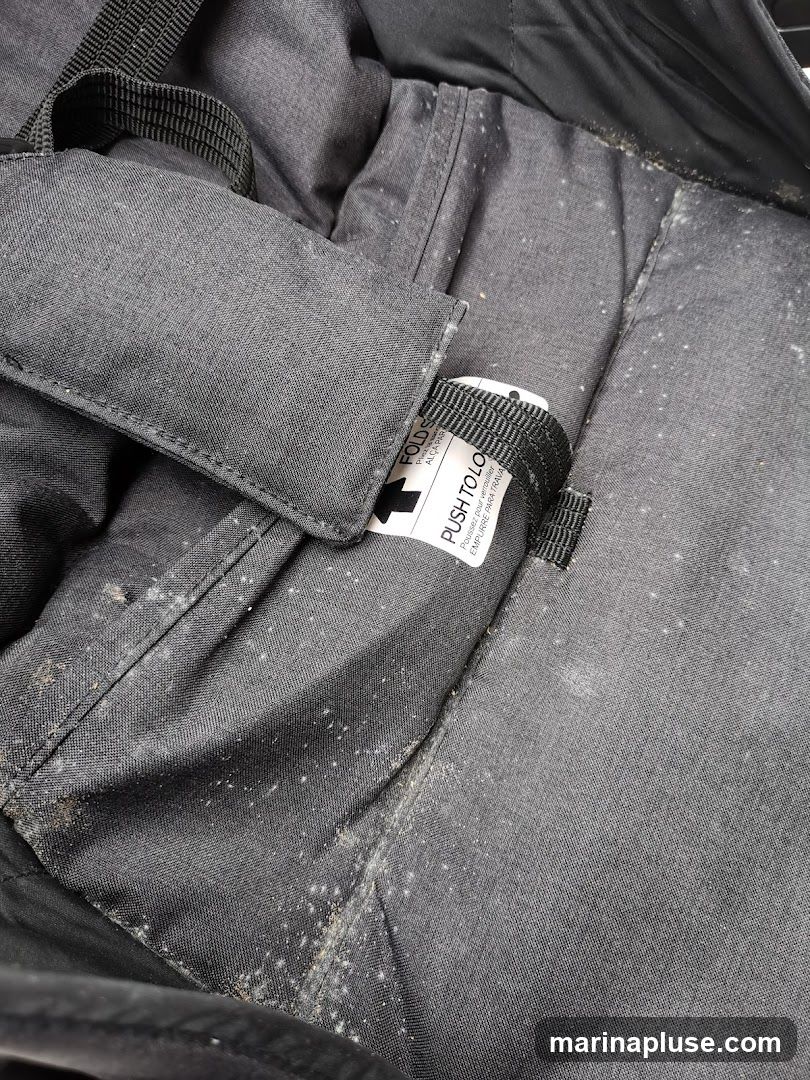 The image shows the interior of a black fabric item, possibly a bag or stroller, with visible signs of dirt and mold. The fabric is creased and appears worn. A label with text including "PUSH TO LO" and "FOLD" is visible.