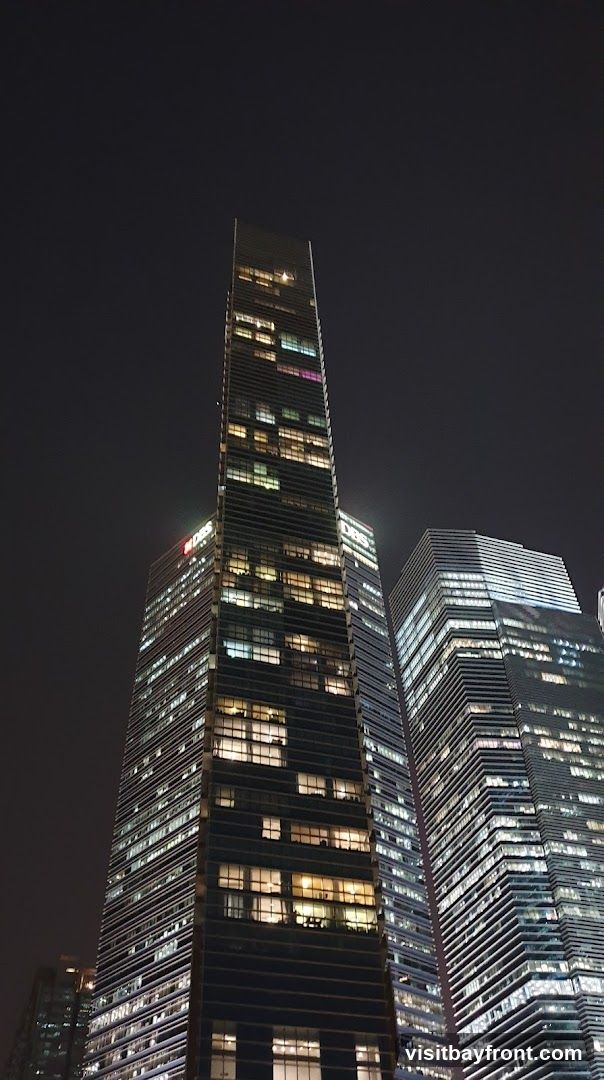A low-angle shot of modern skyscrapers at night, illuminated by numerous windows. The buildings are tall and sleek, with one on the left featuring a prominent sign that reads 'DBS'. The sky is dark, emphasizing the lights of the city.
