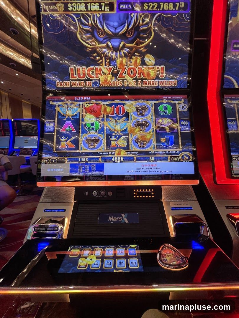 A close-up of a slot machine with a dragon theme. The screen displays "LUCKY ZONE!" and jackpot amounts. The lower screen shows betting options and a timer. The machine has a "Mars X" logo.