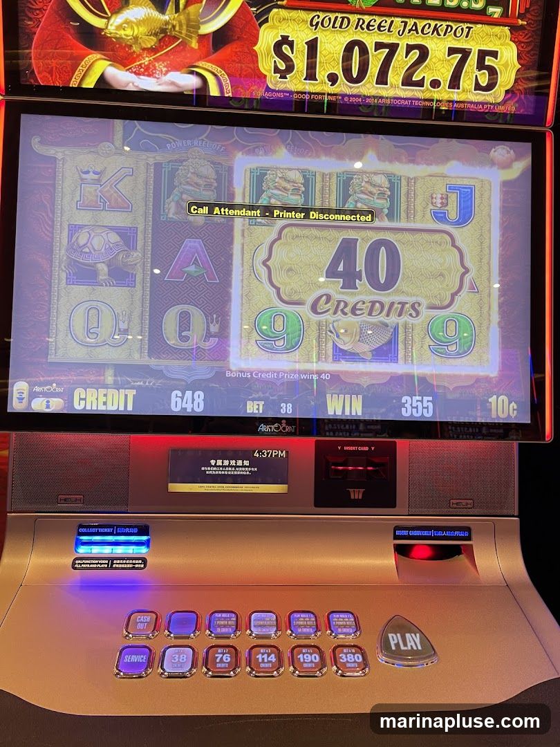 A close-up of a slot machine with a jackpot of $1,072.75 displayed. The screen shows a game in progress with symbols like K, Q, A, J, and 9. A message indicates "Call Attendant - Printer Disconnected." Below the screen are various buttons for betting, service, and playing.