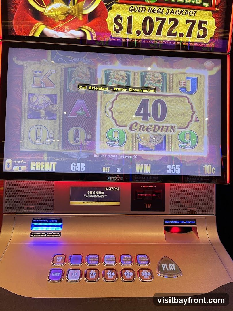 A close-up of a slot machine with a jackpot of $1,072.75 displayed. The screen shows a game in progress with symbols like K, Q, A, J, and 9. A message indicates "Call Attendant - Printer Disconnected." Below the screen are various buttons for betting, service, and playing.
