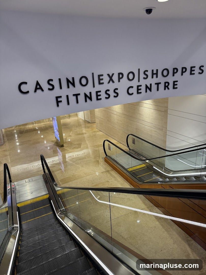 A sign reads "CASINO|EXPO|SHOPPES FITNESS CENTRE" above a view of escalators in a modern, well-lit interior. The floor is polished marble, reflecting the lights and signage.
