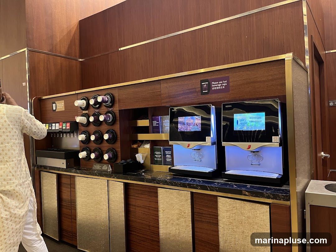 A beverage station with two Nescafe machines, a soda dispenser, and a cup dispenser. The Nescafe machines have screens displaying different beverage options. A sign above the cup dispenser reads "Please use hot beverage cups".