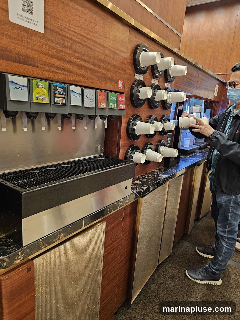 A self-serve beverage station with multiple soda dispensers and cup holders. A person wearing a mask is taking a cup. The dispensers offer water, Heaven & Earth, Minute Maid Refresh, Soda, Coca-Cola, and Sprite.