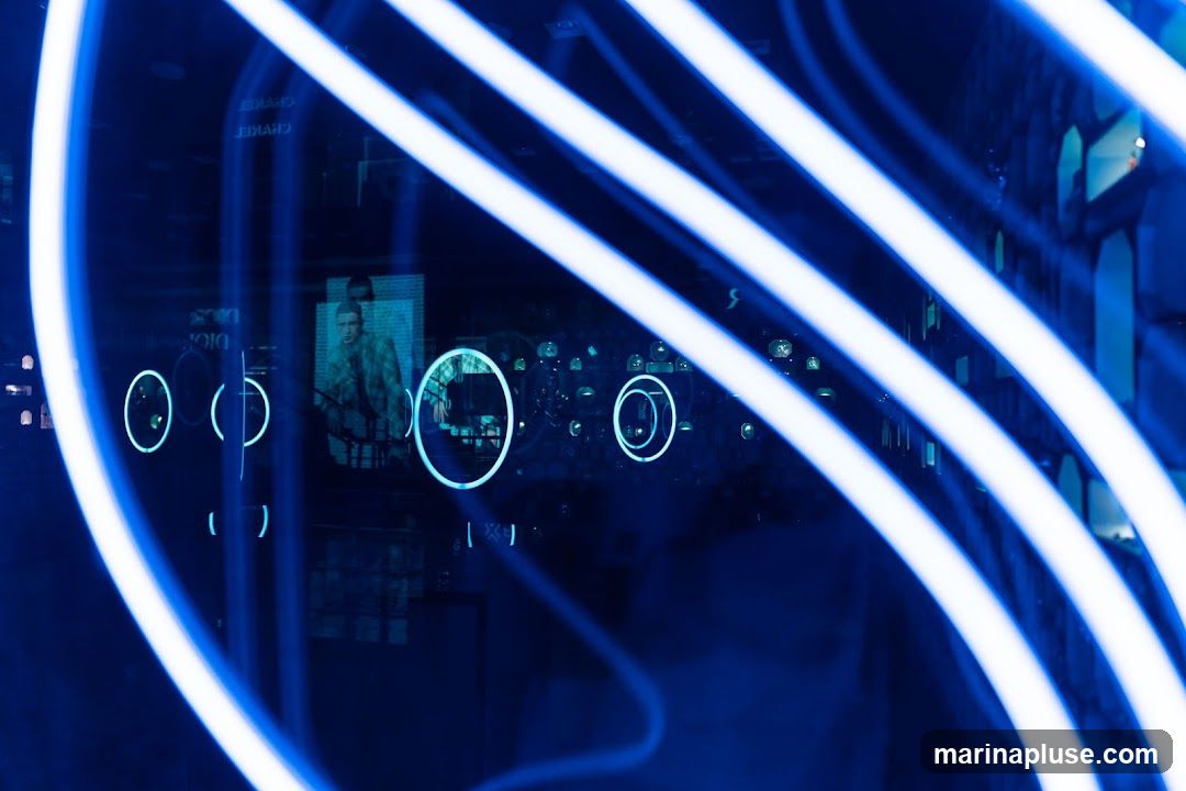 The image features a dark, abstract scene dominated by bright, white neon lights that curve and streak across the frame. These lights create a sense of movement and energy. Reflected in the dark surface, possibly a window or display, are glimpses of what appears to be a store interior. Visible elements include a poster or screen displaying a person in a suit, circular light accents, and faint text that might be brand names. The overall impression is modern and possibly commercial, with a focus on visual display and lighting.