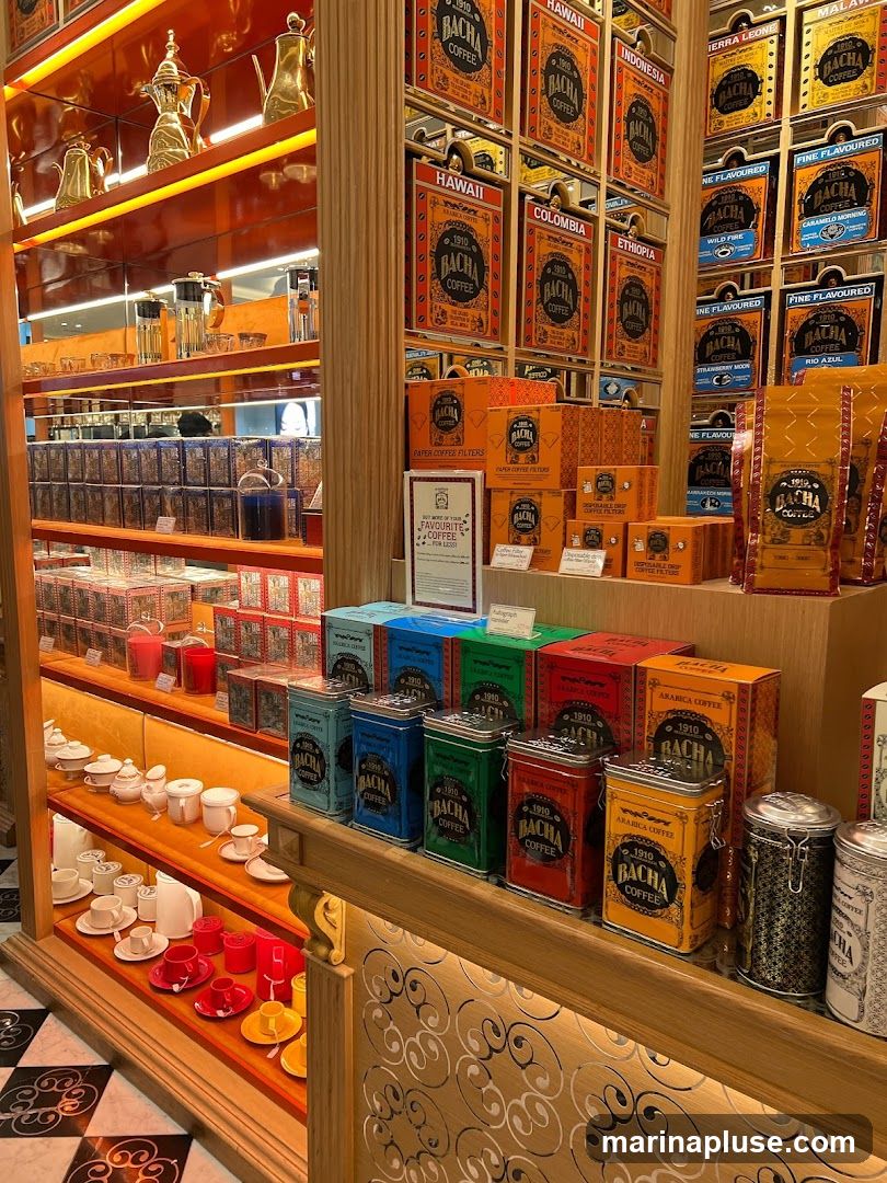 A well-lit display of coffee and tea products. Shelves are stocked with colorful tins and boxes featuring the 'Bacha Coffee' logo and various coffee origins like Hawaii, Colombia, and Ethiopia. Also visible are tea sets, teapots, and other serving ware. The overall aesthetic is elegant and inviting, with warm lighting and decorative shelving.