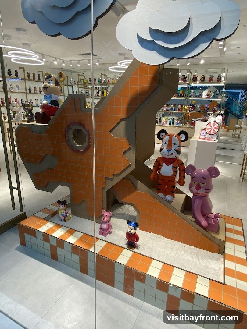 A window display features a large, orange, dragon-like structure made of cardboard. Several collectible toys, including characters resembling Mickey Mouse, a tiger, and a pink bear, are placed on and around the structure. The background shows shelves filled with more collectible toys.