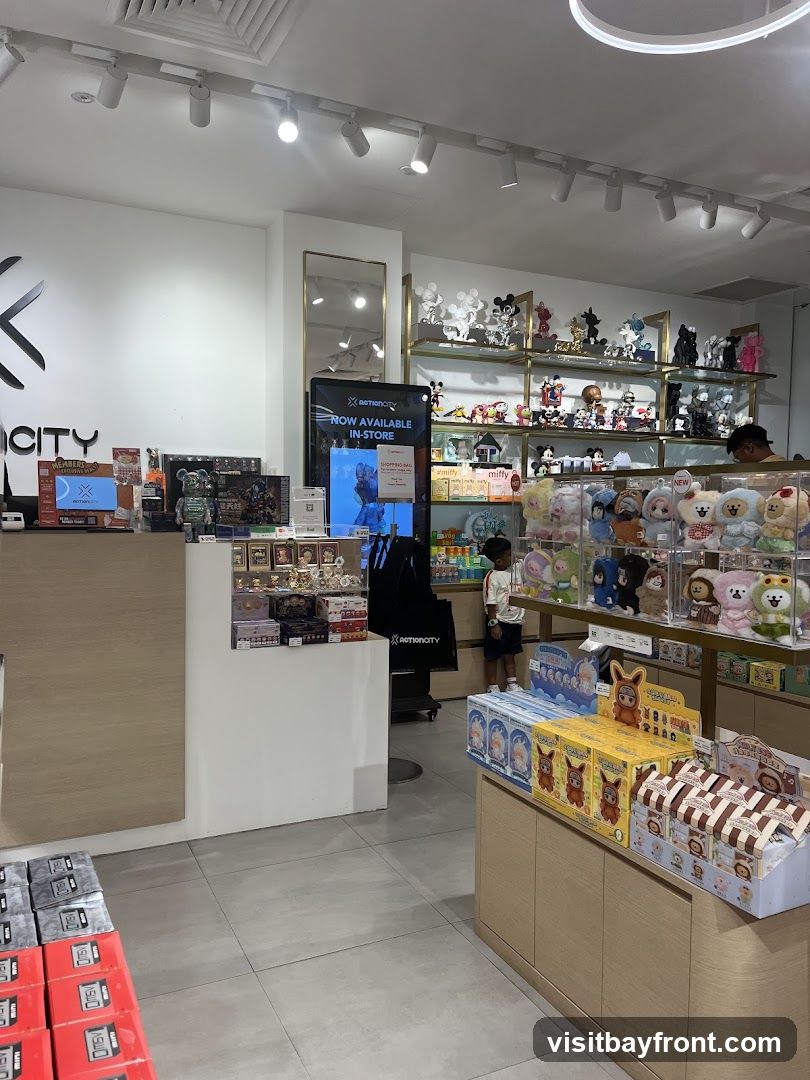The interior of a toy store is filled with various collectible toys and merchandise. Shelves are stocked with figures, plush toys, and boxed items. A digital display shows "NOW AVAILABLE IN-STORE". A child is looking at the merchandise.