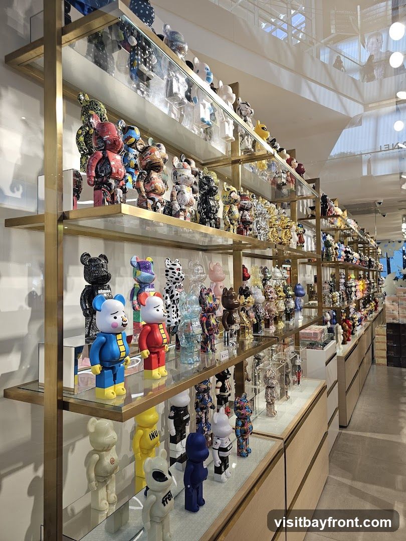 A retail store interior featuring multiple shelves filled with various collectible figurines, primarily in the style of Bearbrick toys. The figurines are displayed in a wide array of colors, patterns, and designs. Some shelves also show boxes and other merchandise. The store appears modern with clean lines and ample lighting.