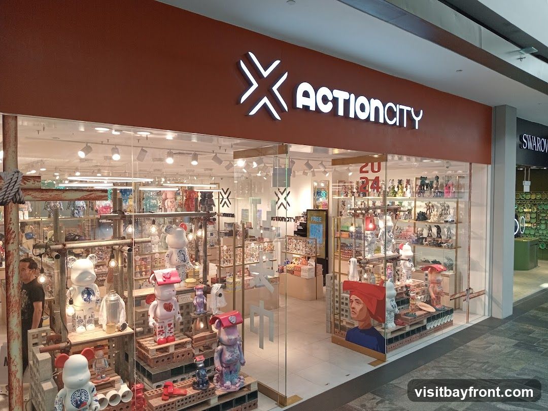 The exterior of a store called Action City, featuring a large display window filled with various collectible toys and figures. The store's name is prominently displayed in illuminated white lettering above the entrance. The facade is a warm, reddish-brown color.