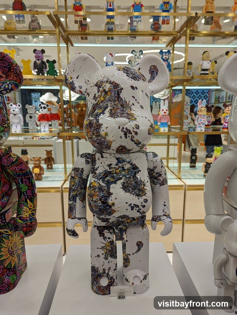 A close-up view of several collectible figurines, prominently featuring a large white bear-shaped figure with abstract paint splatters in various colors. The figurine is displayed in what appears to be a retail setting, with shelves filled with other similar collectible toys in the background. A small price tag is visible at the base of the main figurine.