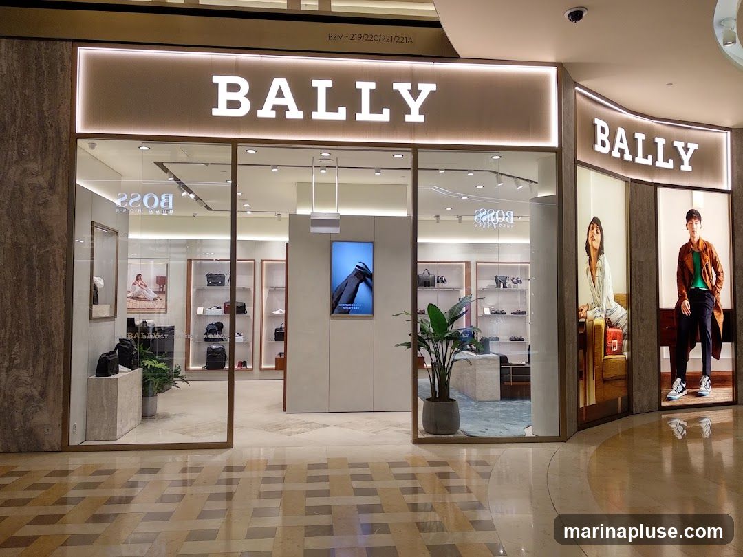 The exterior of a Bally store with large glass windows and illuminated signage. Inside, shelves display handbags and shoes. Mannequins are visible in the windows.