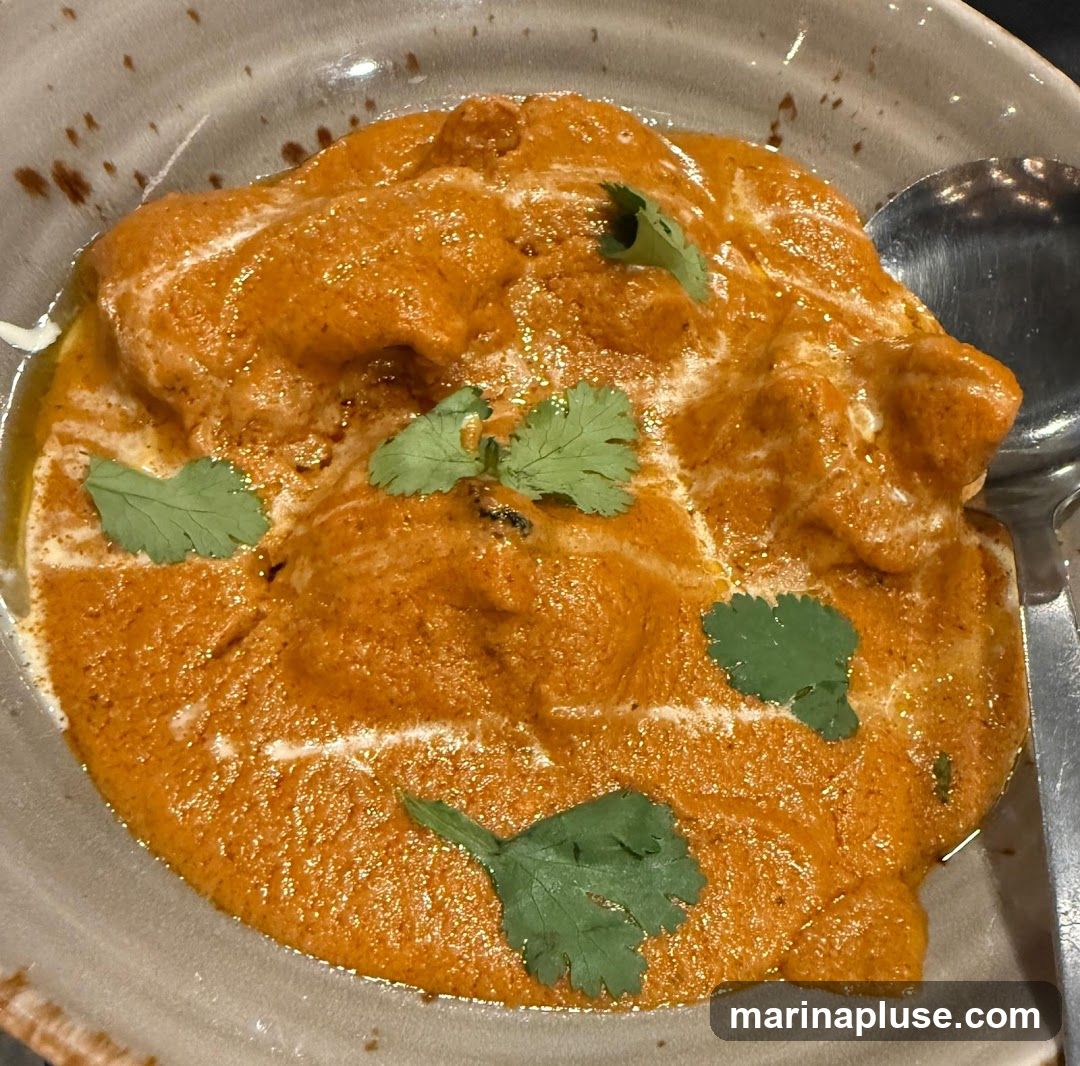 A close-up shot of chicken tikka masala in a bowl, garnished with cilantro. A spoon is visible on the right side of the bowl.