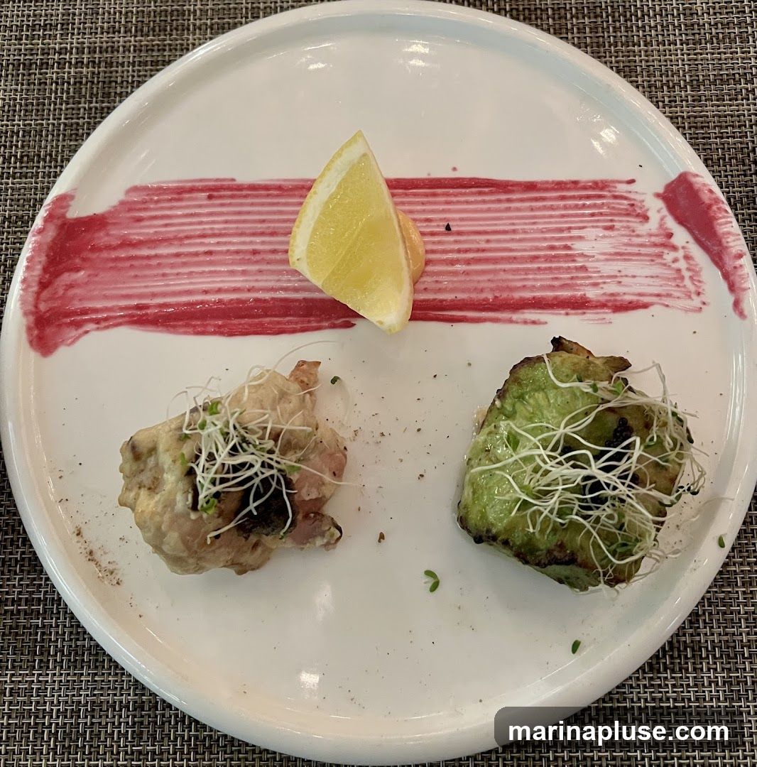 A white plate holds two small portions of food, garnished with sprouts and a lemon wedge. A streak of red sauce is painted across the plate.