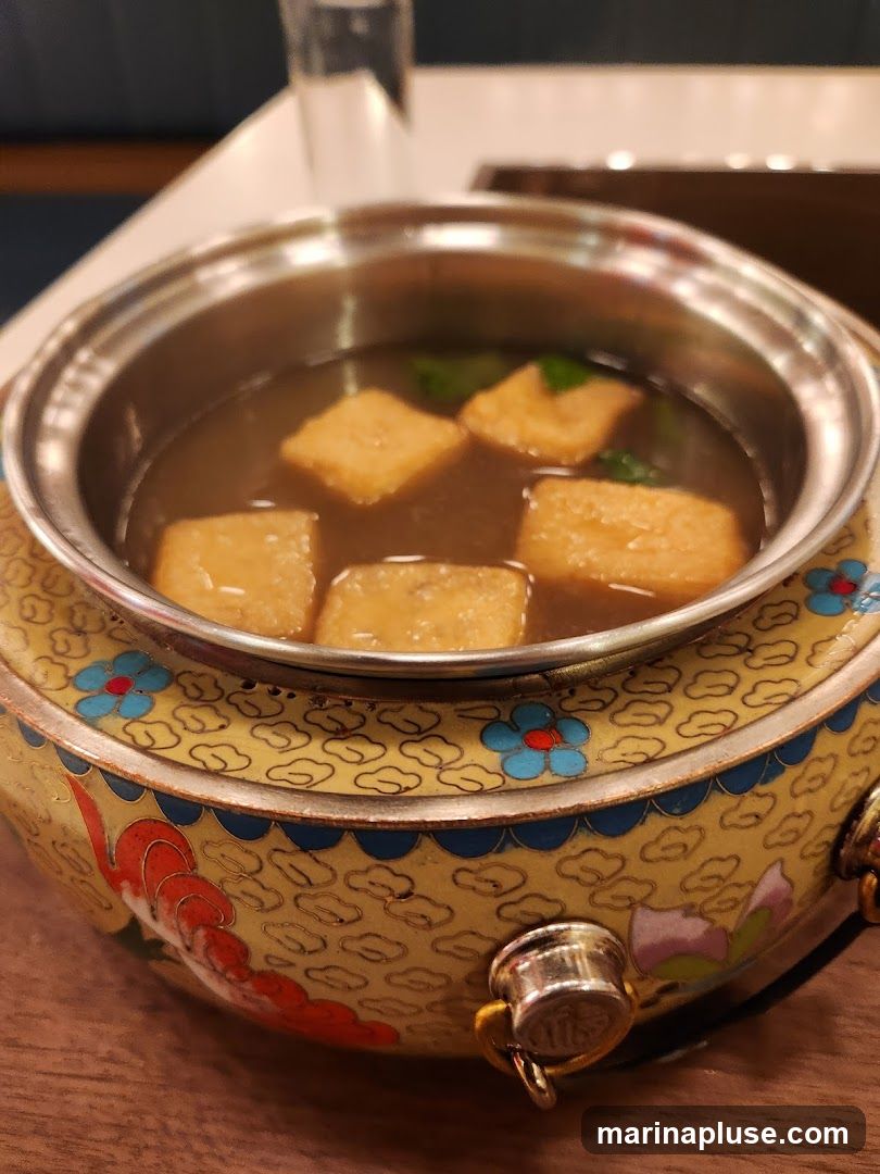 A close-up shot of a small metal pot filled with broth and several pieces of fried tofu. The pot is decorated with a yellow base and blue and red floral patterns.