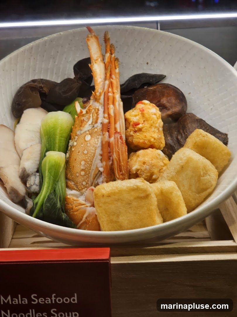 A bowl of Mala Seafood Noodles Soup with a lobster, fish slices, bok choy, mushrooms, fish balls, and fried tofu.