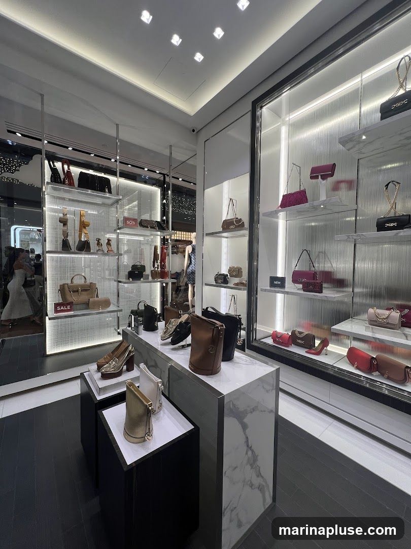 A well-lit retail display showcasing a variety of designer handbags and shoes. The merchandise is arranged on shelves and display stands with a marble-effect finish. Some items are highlighted with "SALE" and "NEW" tags.