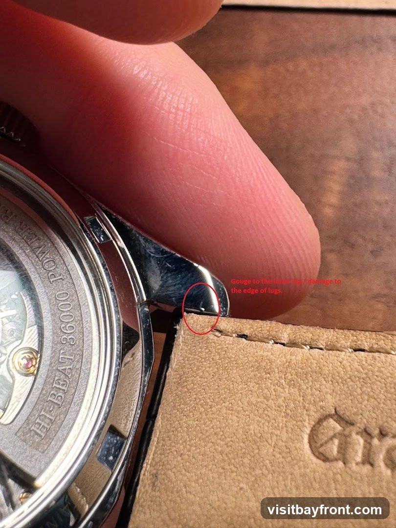 A close-up image shows a finger pressing on the lug of a watch. A red circle highlights a gouge or damage to the edge of the lug. Text indicates "Gouge to the lower lug / damage to the edge of lugs." The watch case has visible text: "HI-BEAT 36000. POWER R". The watch strap is made of light brown leather with visible stitching.