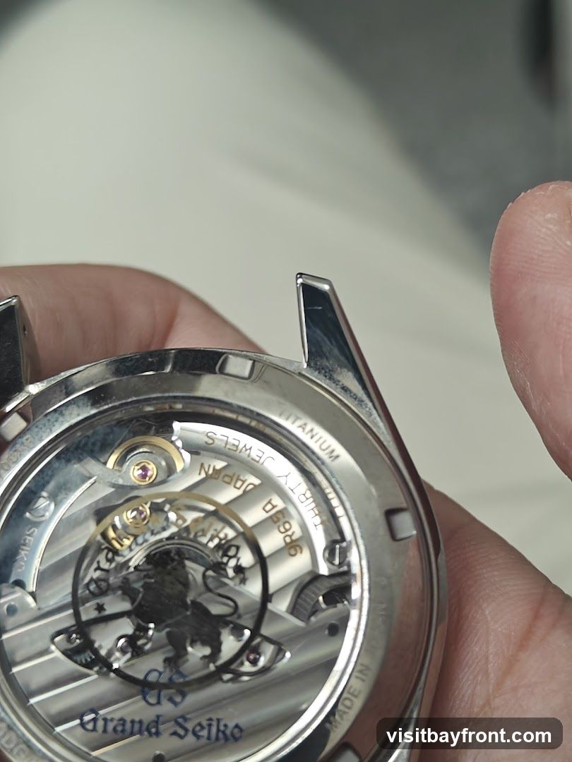 A close-up view of the intricate movement of a Grand Seiko watch, showcasing the detailed craftsmanship and branding. The watch case is made of titanium. The movement is labeled with 'SEIKO', 'JAPAN', 'THIRTY JEWELS', '9R65A', and 'Grand Seiko'. A lion emblem is visible in the center.
