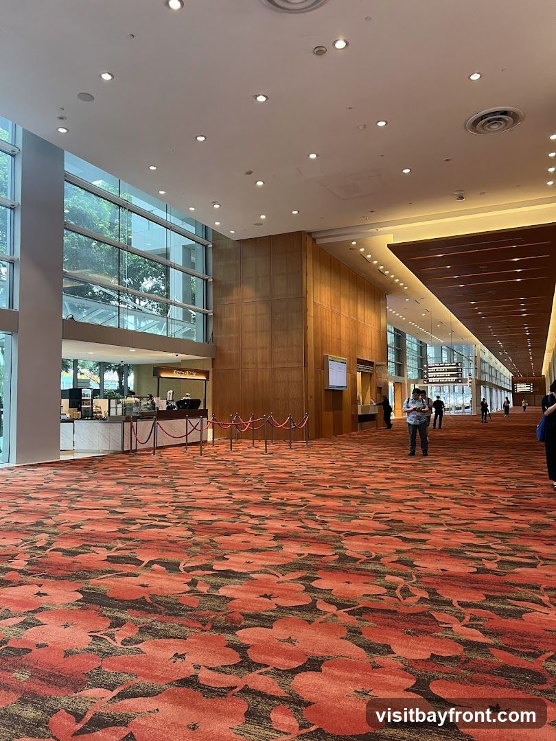 A wide, well-lit hallway with a vibrant floral carpet. On the left, a counter area with a sign that reads "Fresh Brew". Several people are walking in the distance. The architecture features large windows and wooden paneling.