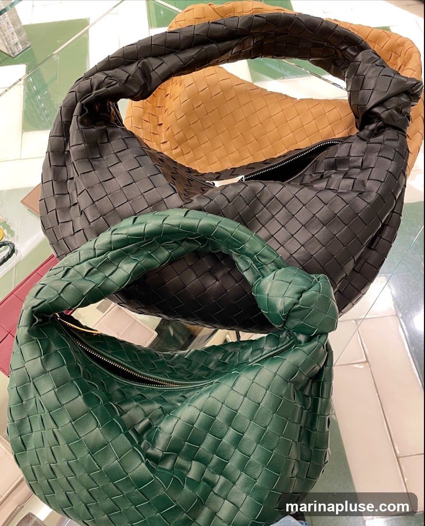 Three woven leather handbags are displayed. The handbag in the foreground is green, the middle one is black, and the one in the background is tan. The bags have a knotted detail on the strap.