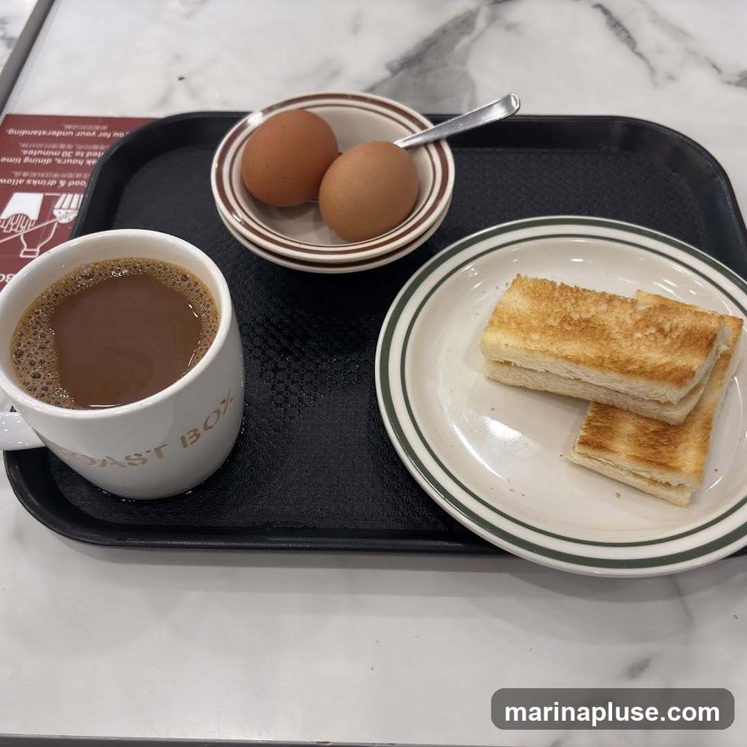 A tray with a mug of coffee, two hard-boiled eggs, and two slices of toast. The mug has "TOAST BOX" printed on it. A small sign with text in English and Chinese is visible in the background.