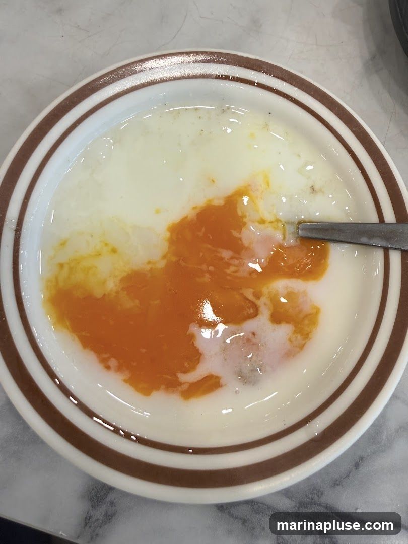 A close-up shot of two soft-boiled eggs in a white bowl with brown stripes. The egg whites are cooked, and the yolks are runny and bright orange. A spoon is visible on the right side of the bowl.