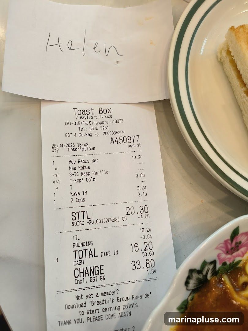 A receipt from Toast Box with a handwritten name 'Helen' at the top. The receipt details food items purchased, including Mee Rebus Set, S-TC Rasp Vanilla, T-Kopi Cold, Kaya TR, and 2 Eggs. It also shows a discount and the total amount paid. A portion of a sandwich and a dish with sauce are visible on the side.