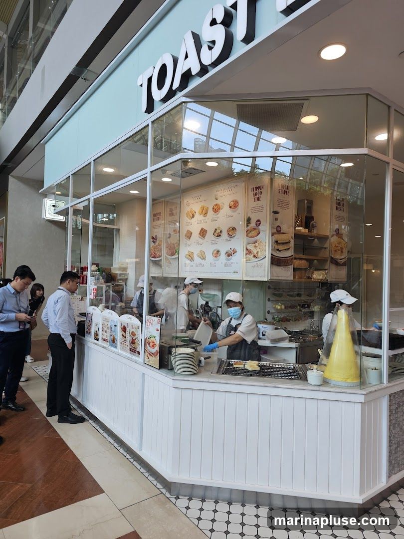A bright and clean shop front with large glass windows, displaying a menu and food items. The shop's name,