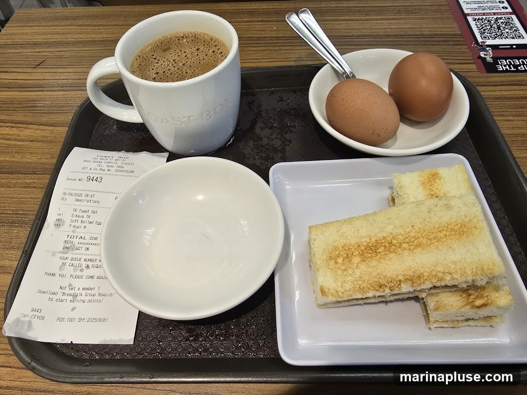 A tray with a cup of coffee, two soft-boiled eggs, and toast. A receipt is also on the tray. The coffee cup has the logo "Toast Box" embossed on it.