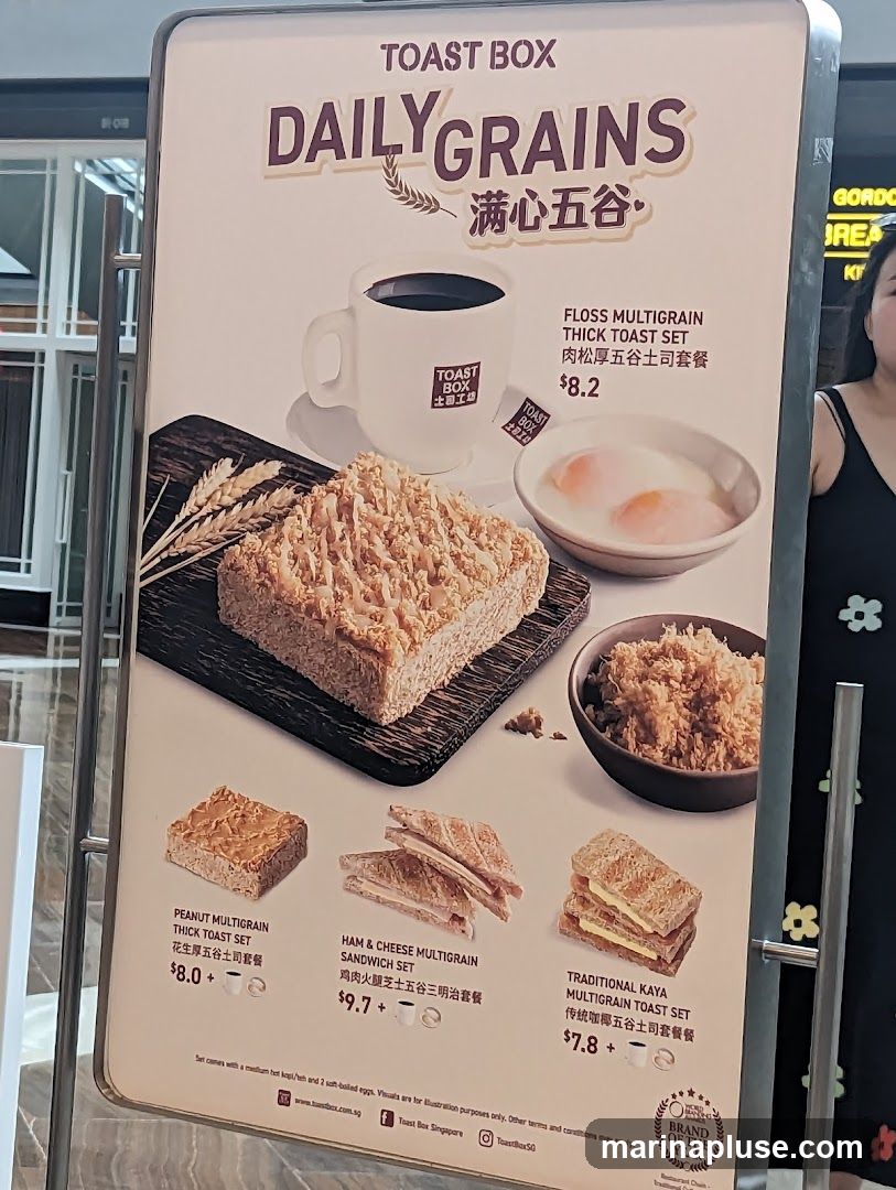 A menu board for Toast Box featuring their Daily Grains sets, including thick toast sets and sandwich sets with coffee and soft-boiled eggs.