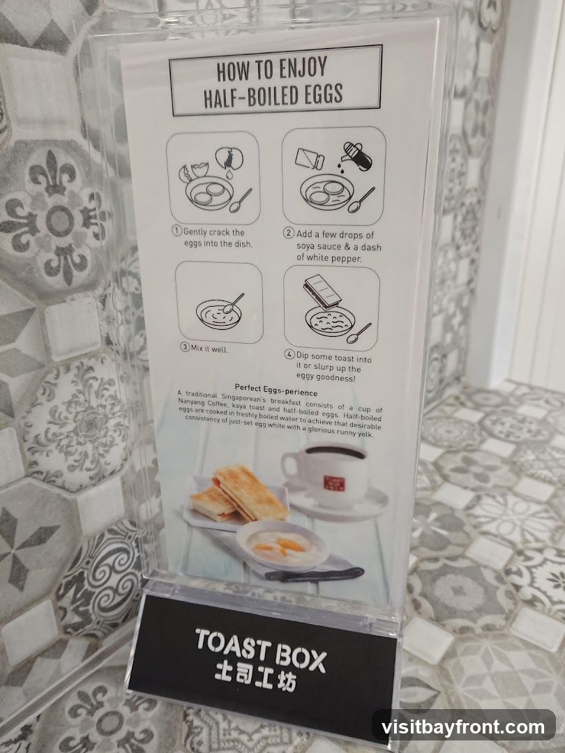 A sign with instructions on how to enjoy half-boiled eggs, including steps like cracking eggs, adding soy sauce and pepper, mixing, and dipping toast. It also describes the perfect eggs-perience of a traditional Singaporean breakfast with Nanyang Coffee and kaya toast. The sign has the 'TOAST BOX' logo at the bottom.