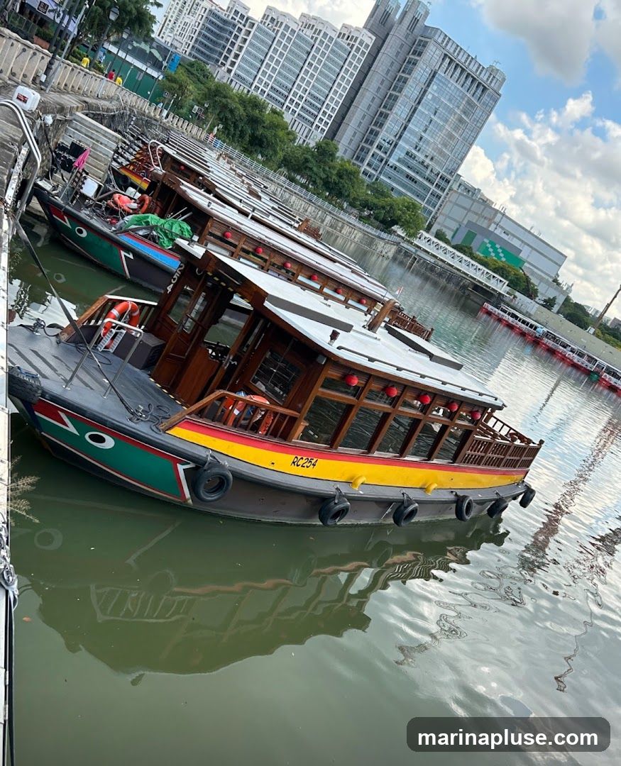 A line of traditional wooden boats with red lanterns are docked along a stone quay. The boats are painted with colorful stripes and have wooden cabins. In the background, modern high-rise buildings dominate the skyline, reflecting in the water. The sky is partly cloudy.