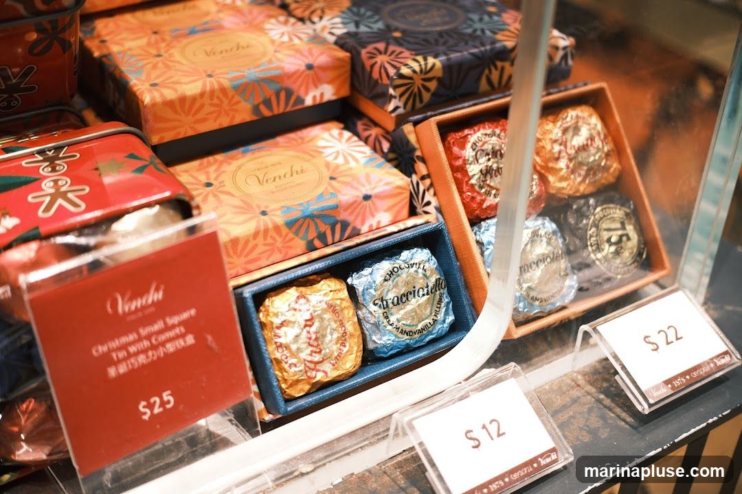 A display of Venchi chocolates in decorative boxes and tins. Some chocolates are individually wrapped in foil. Price tags are visible for some items.
