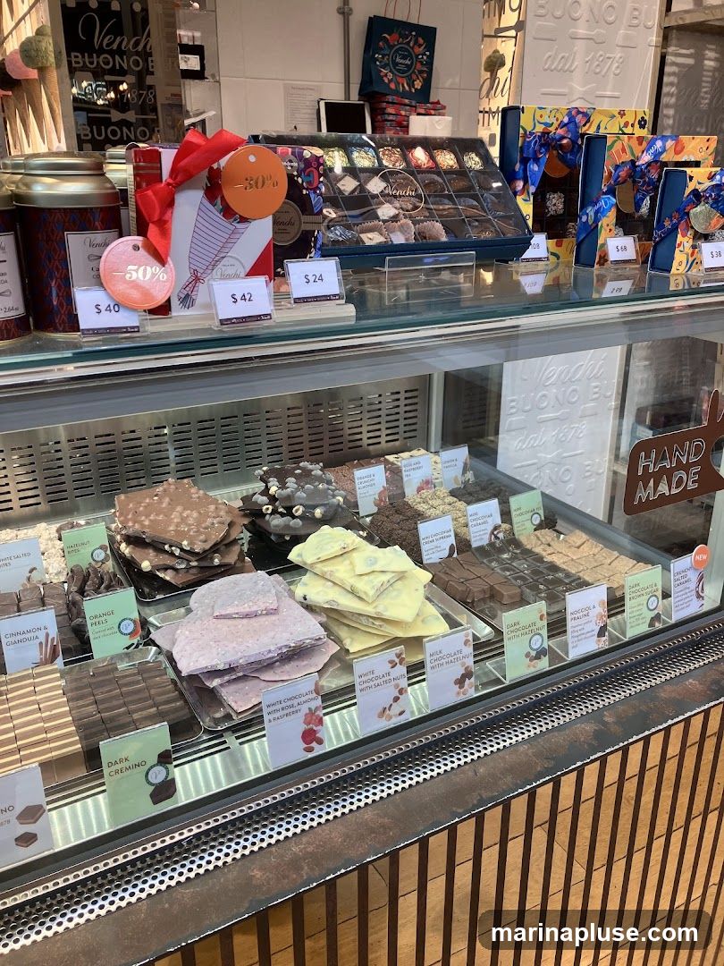 A display case filled with various chocolates and chocolate bars from Venchi. There are also gift boxes and tins of chocolate. Some items have discount tags.