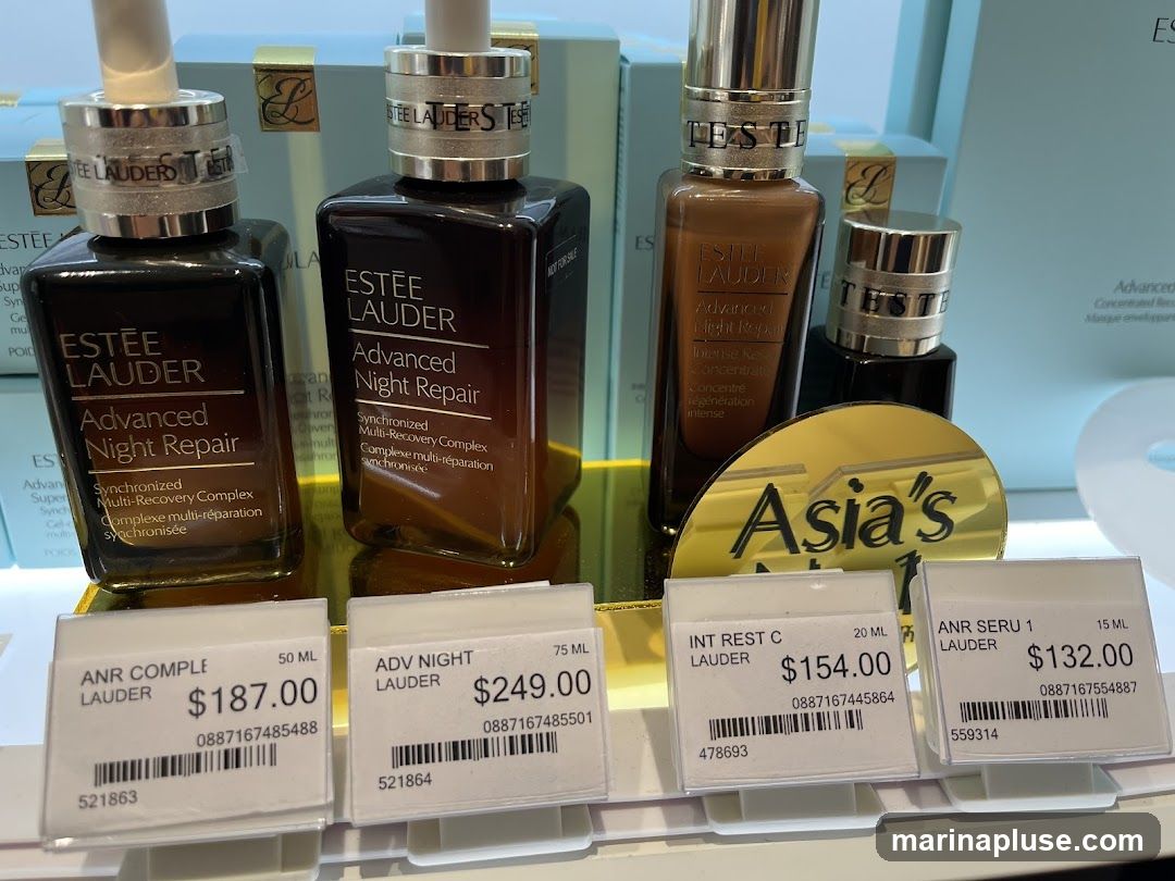 A display of Estee Lauder Advanced Night Repair products with price tags. The products are in dark brown bottles with gold caps. The price tags show product names, sizes, prices, and barcodes. A golden sign with "Asia's" is visible behind the bottles.