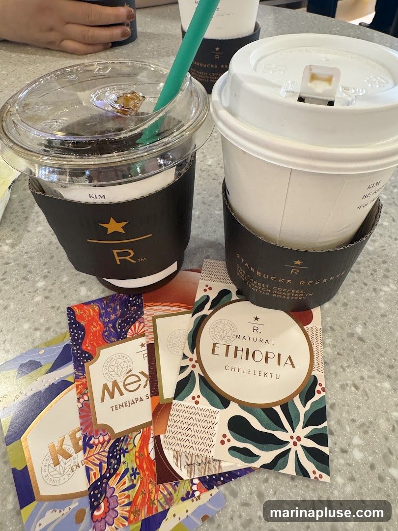 Two Starbucks Reserve coffee cups and several small coffee sample cards are arranged on a speckled countertop. One cup is a clear plastic cup with a green straw and ice, and the other is a white paper cup. Both cups have black sleeves with the Starbucks Reserve logo. The sample cards are colorful and feature designs and text indicating coffee origins such as "Ethiopia Chelelektu" and "Mex Tenejapa S."