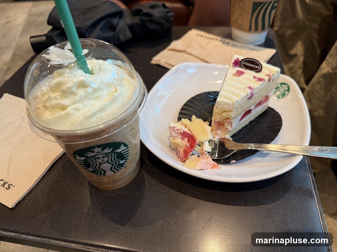 A close-up shot of a Starbucks Frappuccino with whipped cream and a slice of strawberry cake on a white plate. The Starbucks logo is visible on the cup and the plate. A fork is on the plate, and a napkin with the Starbucks logo is to the left of the cup.