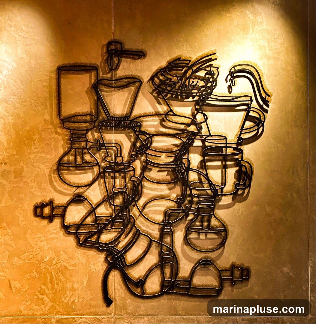 A metal wire art installation depicting various coffee brewing methods, including siphon brewers, pour-over devices, and cups, is mounted on a textured wall. The artwork is illuminated by spotlights, casting shadows on the wall.