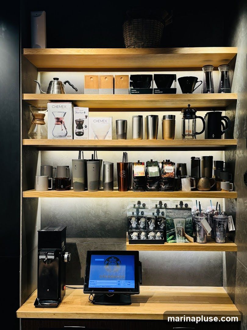 Shelves display various coffee brewing equipment, including Chemex carafes, pour-over sets, French presses, and kettles. Also visible are bags of coffee beans, reusable cups, and small decorative items. A point-of-sale terminal with the Starbucks logo is on the counter, next to a coffee grinder.